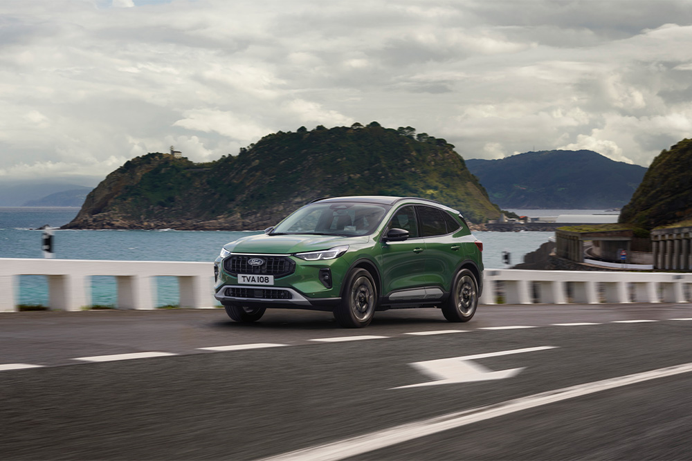 Zöld Ford Kuga öntöltő hibrid autó egy festői úton halad.