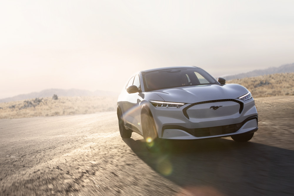 Ezüstszínű elektromos Ford Mustang Mach-E GT halad egy festői úton.