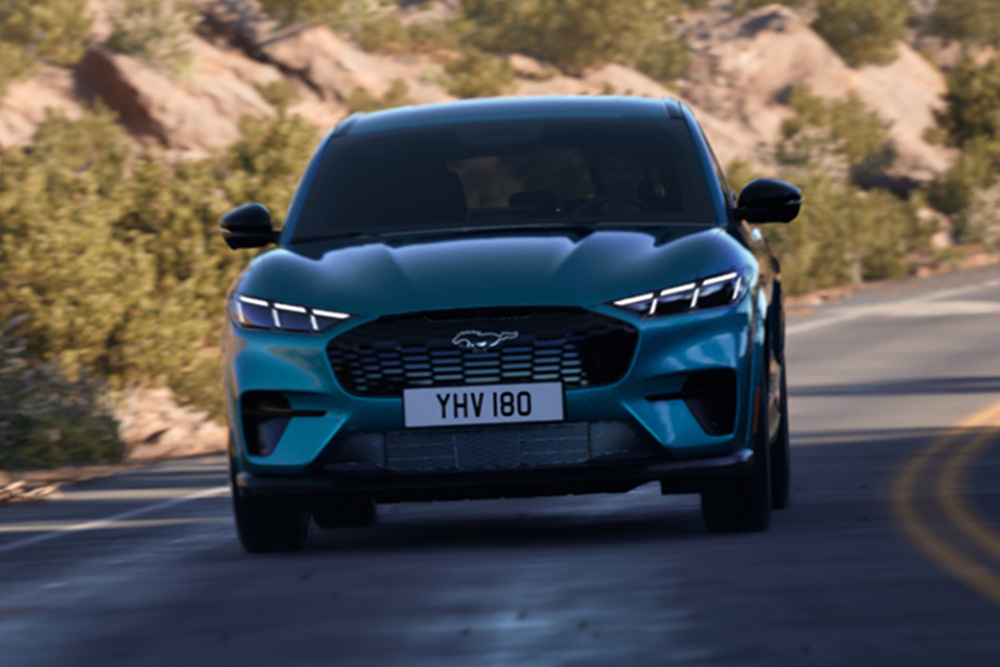 Hegyi úton haladó, kék Ford Mustang Mach-E elölnézetből.