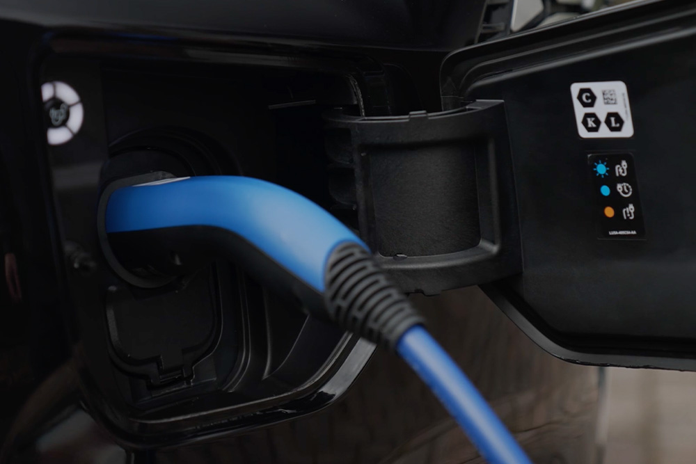 Közelkép egy elektromos jármű töltőcsatlakozójába illesztett kék töltőkábelről.