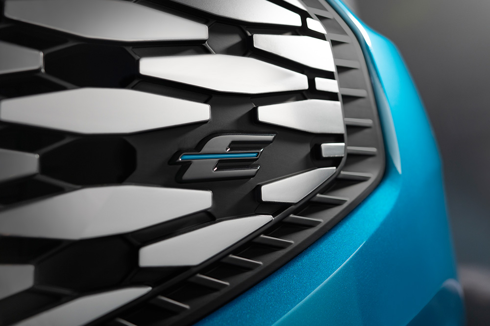 Közelkép a Ford E-Tourneo Custom hűtőrácsáról, rajta a Ford tisztán elektromos járműveit jelző exkluzív kék „E” logóval.