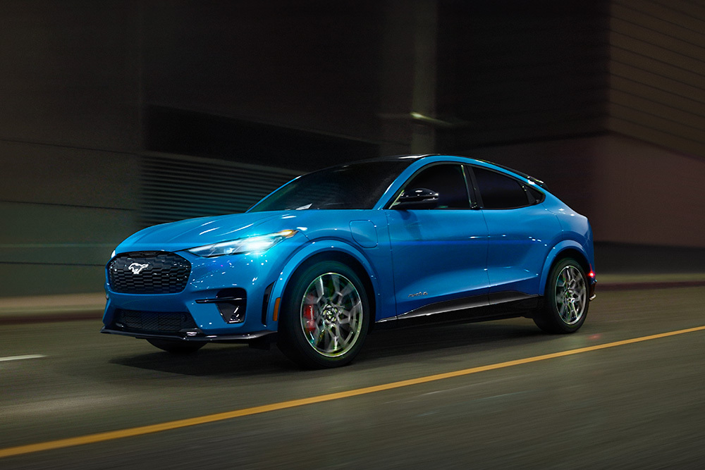 Egy kék Ford Mustang Mach-E GT elektromos sportkocsi, amint a nyílt úton halad.