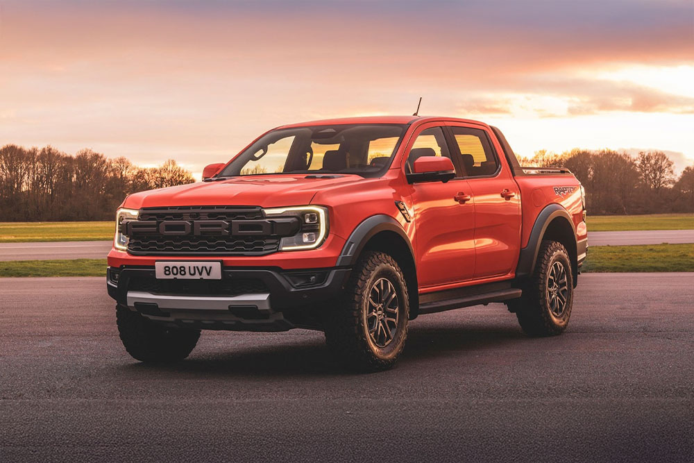 Egy narancssárga Ford Ranger Raptor pickup parkol festői környezetben.