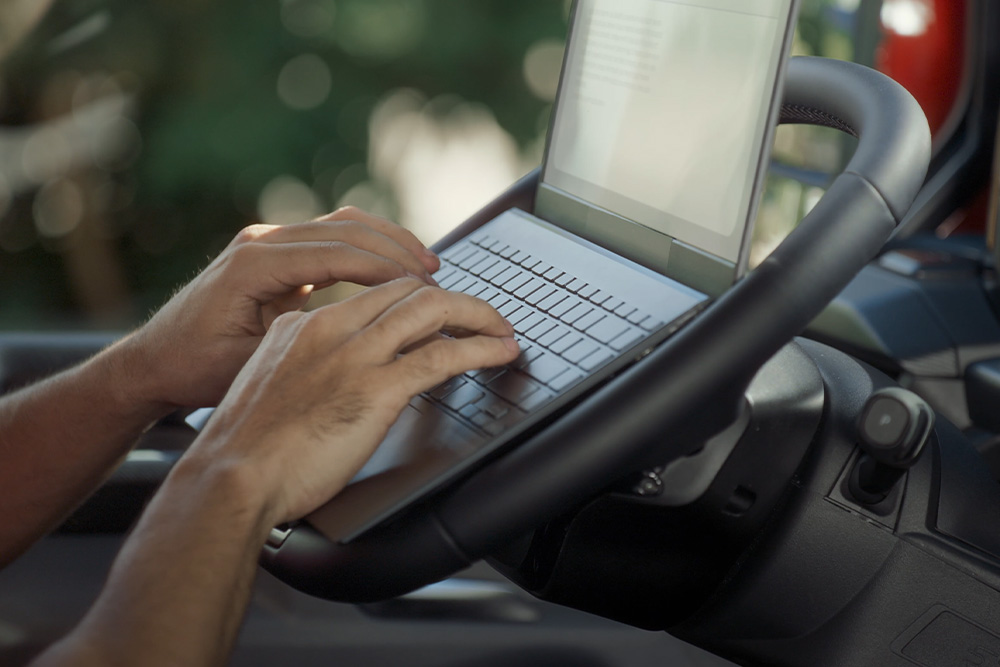 Valaki egy a Ford Tourneo Custom dönthető kormánykerekére helyezett laptopon gépel.
