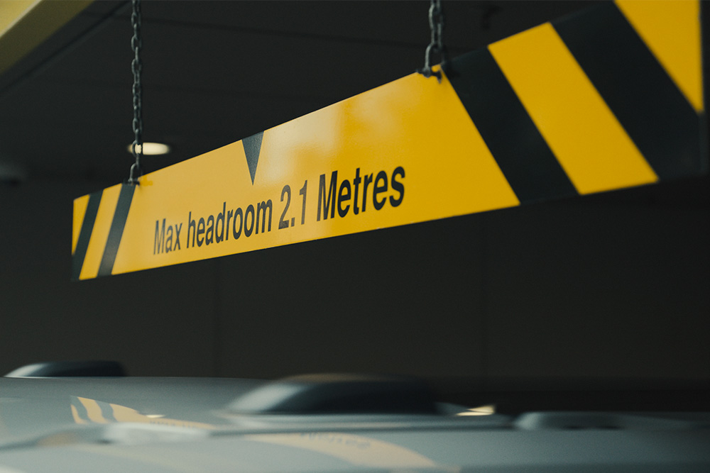 Egy parkolóház sárga-fekete táblája „Max. magasság: 2,1 méter” felirattal.