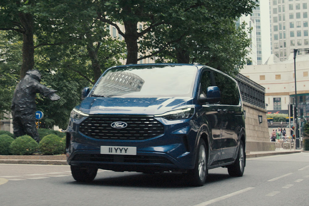 Kék Ford Tourneo Custom egy városban halad az úton.