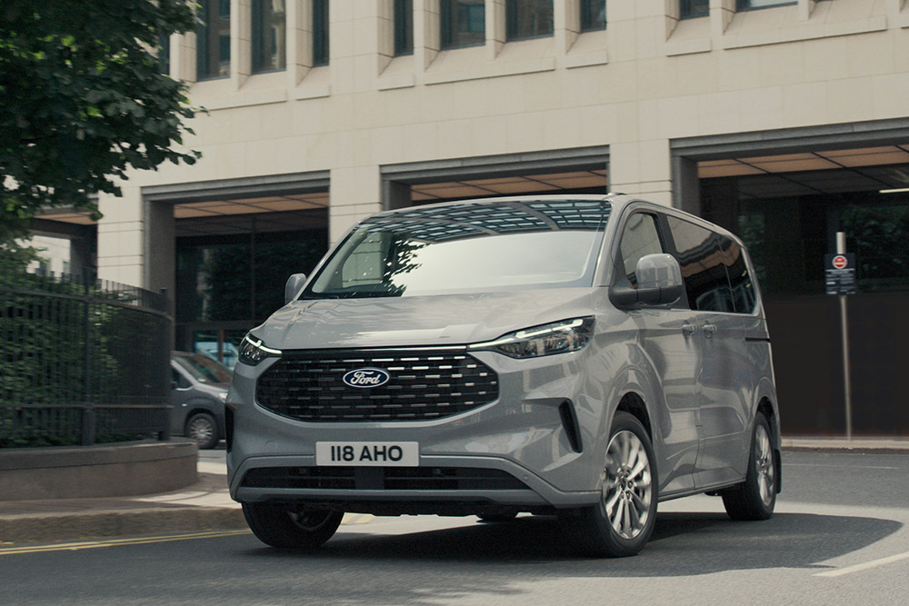 Ezüstszínű Ford Tourneo Custom egy városban halad az úton.