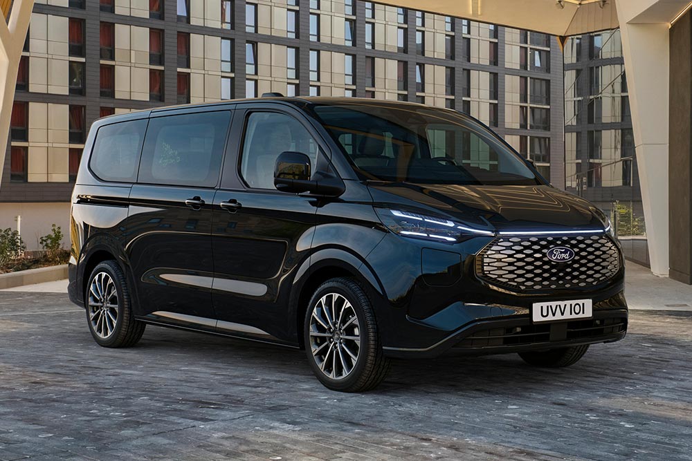Egy fekete Ford E-Tourneo Custom egy modern épület előtt parkol.