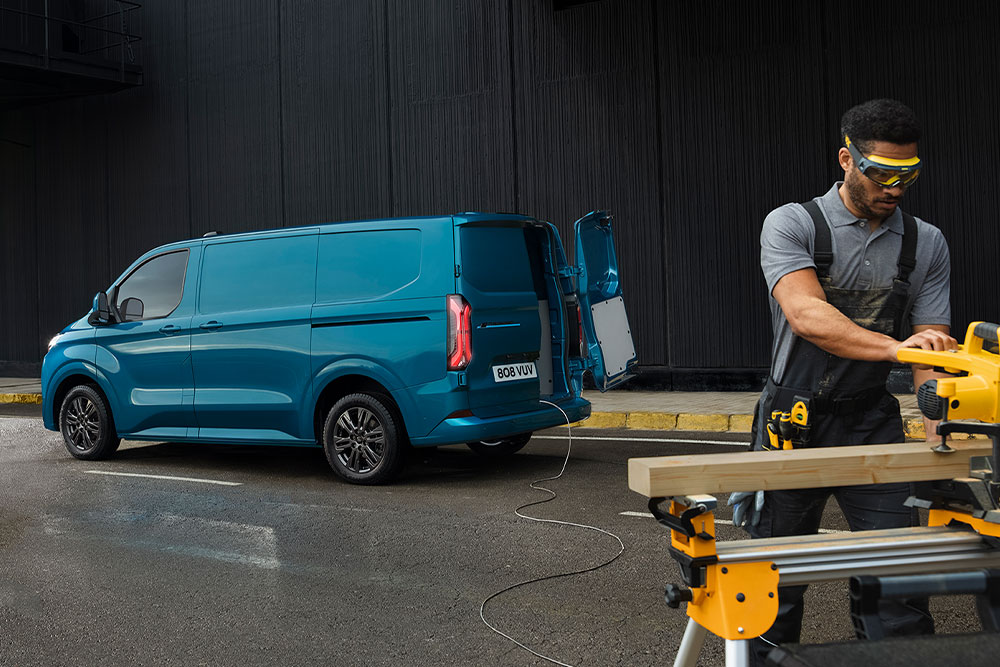 Egy kék Ford E-Transit Custom elektromos áruszállító és egy férfi, aki elektromos szerszámokat használ.