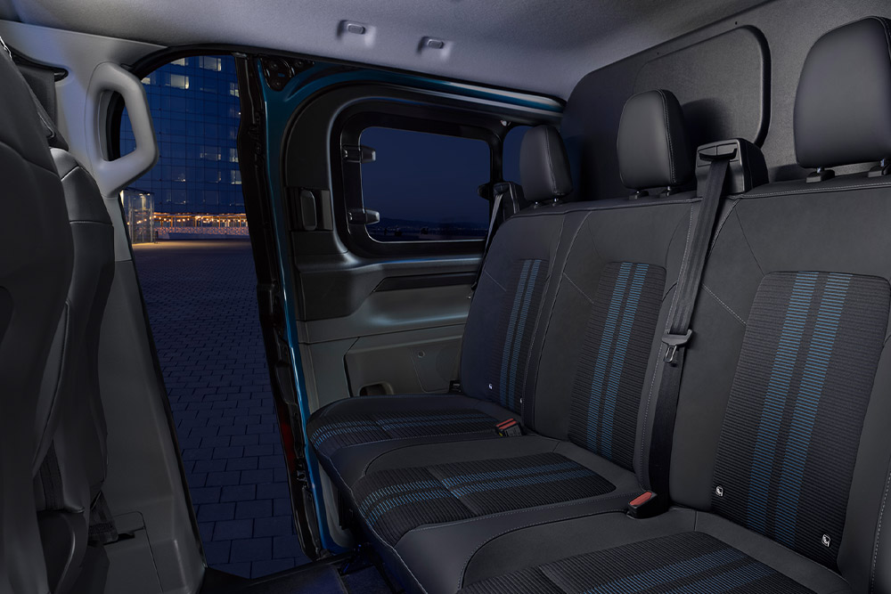 Egy kék Ford E-Transit Custom duplakabinos elektromos személyszállító, hátulnézetből.