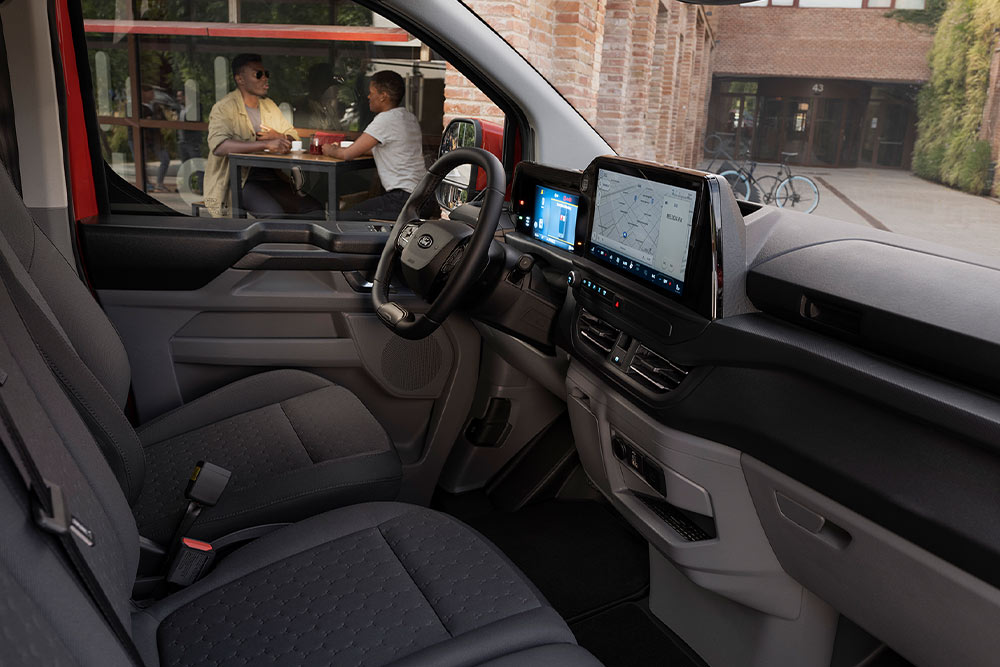 Valaki egy piros Ford E-Transit Custom elektromos áruszállító vezetőülésében ül.