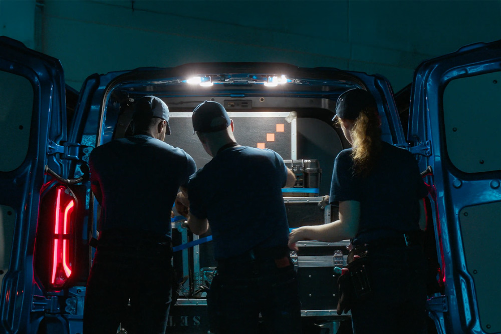 Three people working in the back of a Ford E-Transit Custom van.