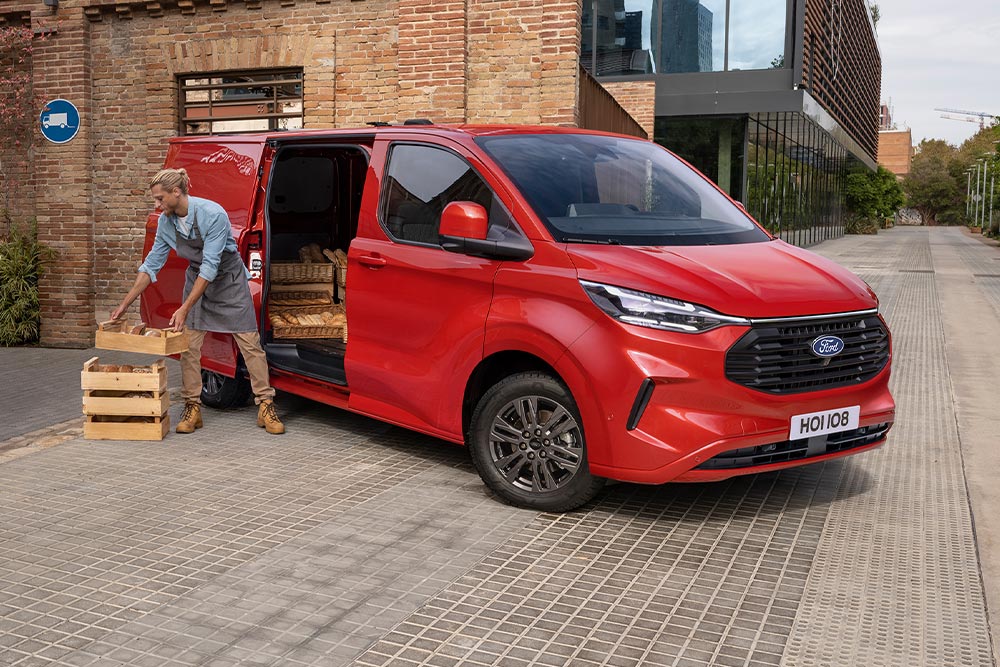 Egy futár csomagokat pakol egy piros Ford Transit Customba.