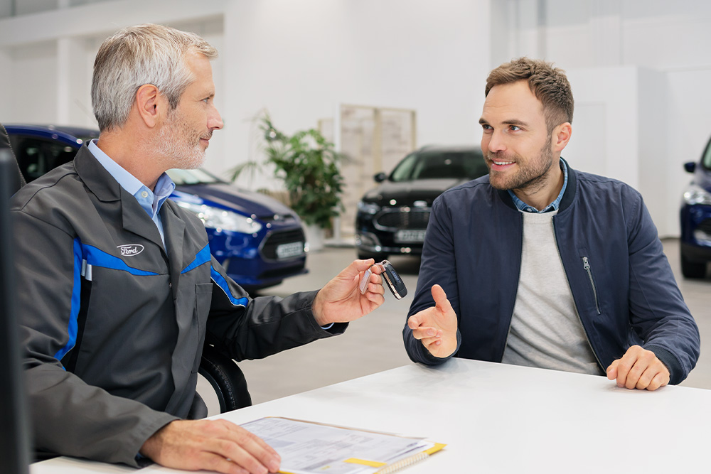 Egy Ford-tanácsadó egy ügyfélnek autókulcsokat ad át, miközben megvitatják a Ford finanszírozási lehetőségeit.