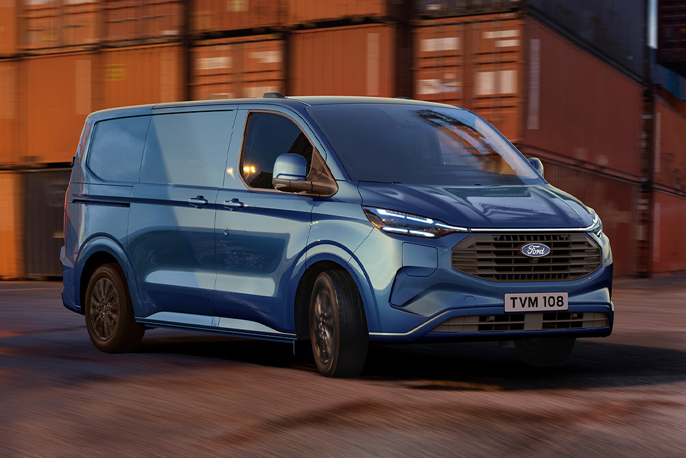 Egy kék Ford Transit Custom plug-in hibrid egy kikötői területen halad át.