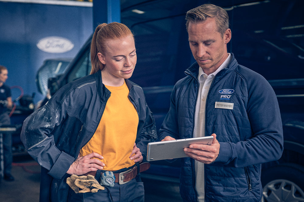 Két szerelő egy garázsban egy Ford E-Transit áruszállító előtt egy tabletet néz.