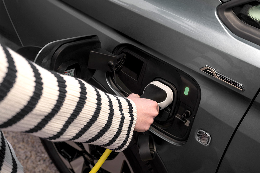 Egy személy egy elektromos töltőkábelt csatlakoztat a Ford Transit Connect plug-in hibrid járműhöz.