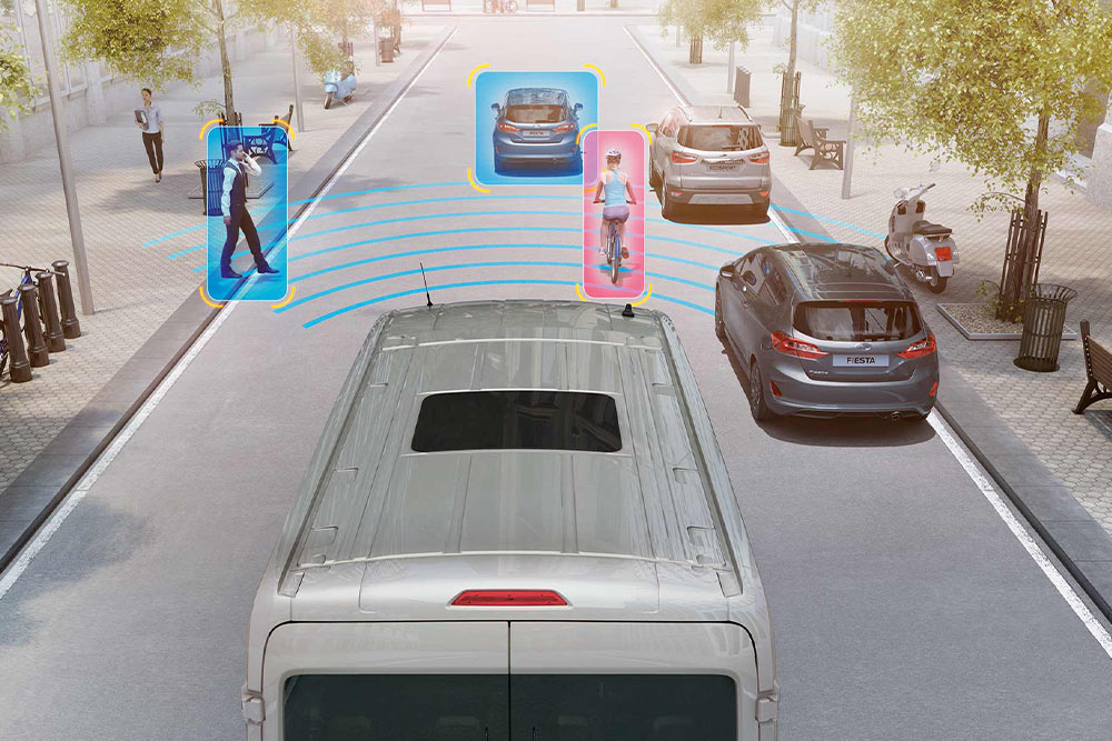 Egy használatban lévő Ford Transit áruszállító vázlata kék és rózsaszín jelölésekkel, amelyek az ütközésmegelőző asszisztenst szemléltetik. 