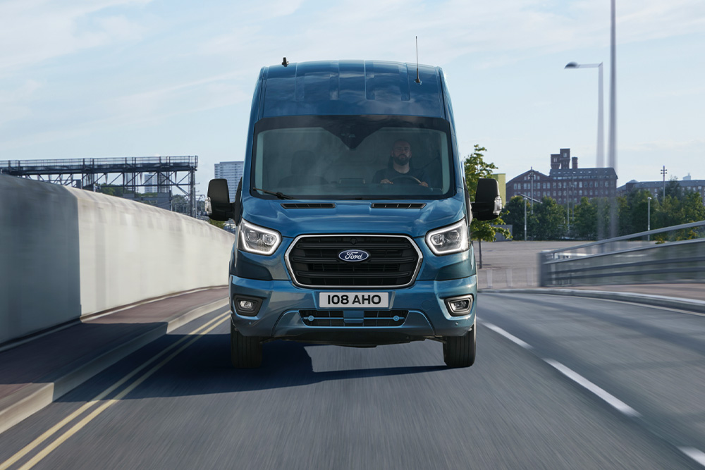 Egy kék Ford Transit Van elölnézete, amint egy úton halad.