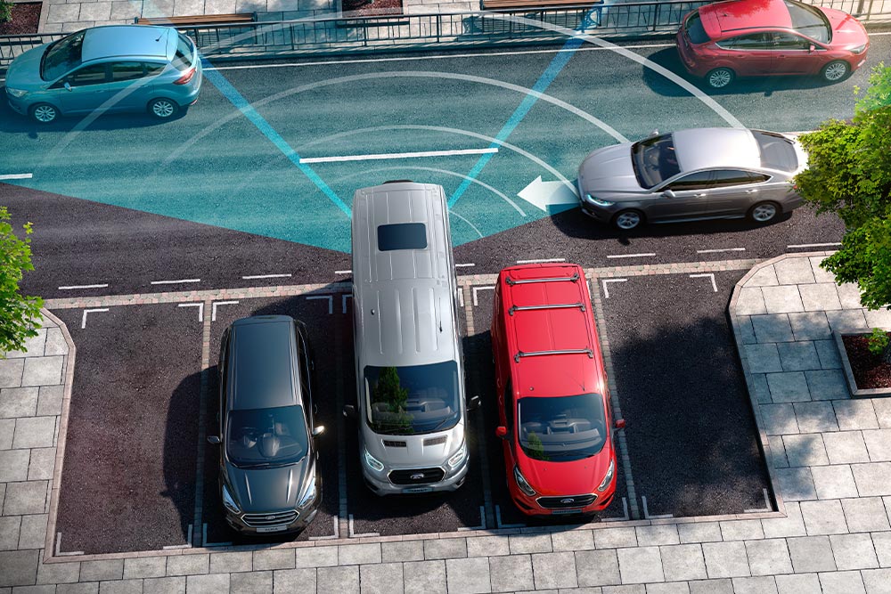 Egy ezüstszínű Ford Transit Van tolat, kék vonalakkal ábrázolva a hátsó parkoló szenzorok működését.