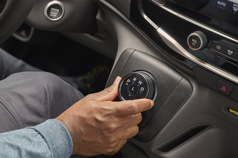 Egy kéz egy Ford Transit fülkés alváz középkonzolján elhelyezett sebességváltó tárcsát kezel.