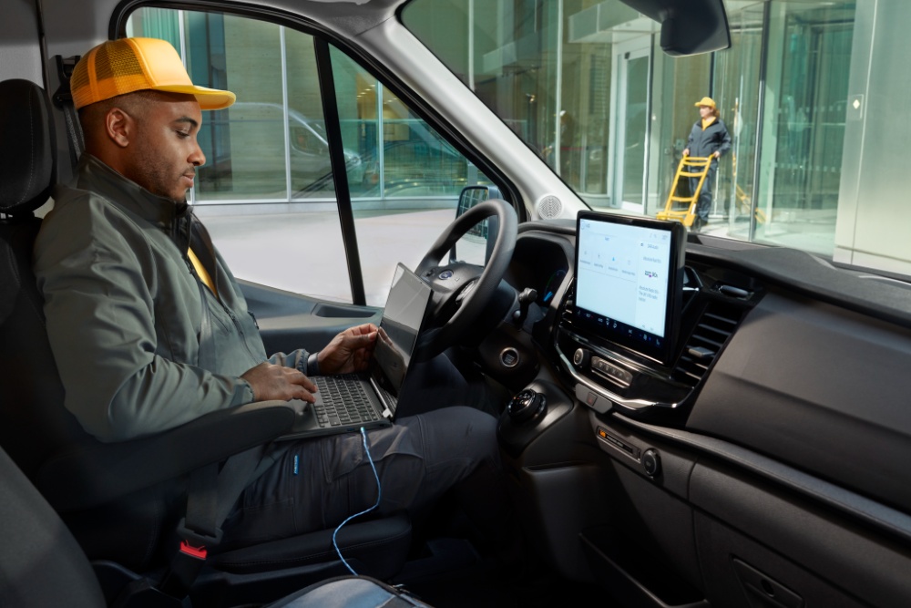 Egy férfi ül egy Ford Transit áruszállító vezetőülésében és laptopot használ.