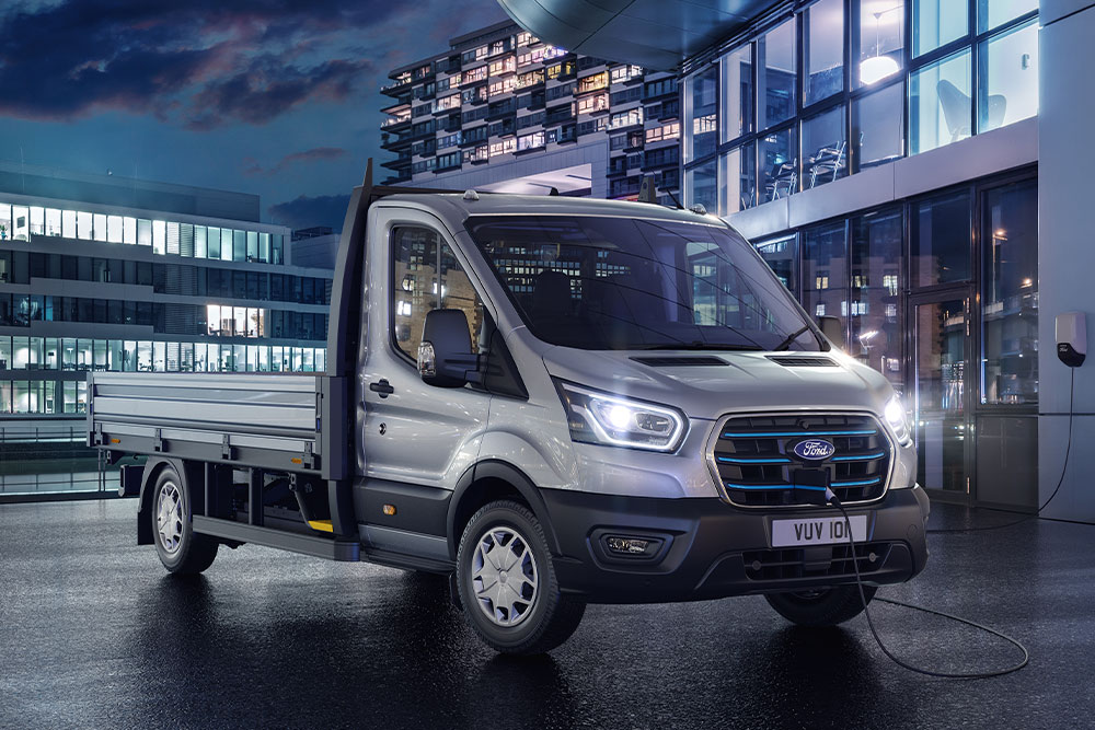Egy ezüstszínű Ford Transit alváz-kabinos kisteherautó áll egy modern épület előtt éjszaka.