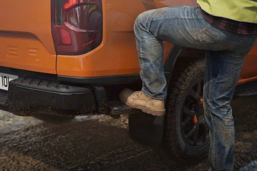 Egy munkást látunk, aki a Ford Ranger Wildtrak beépített hátsó lépcsőjére lép.