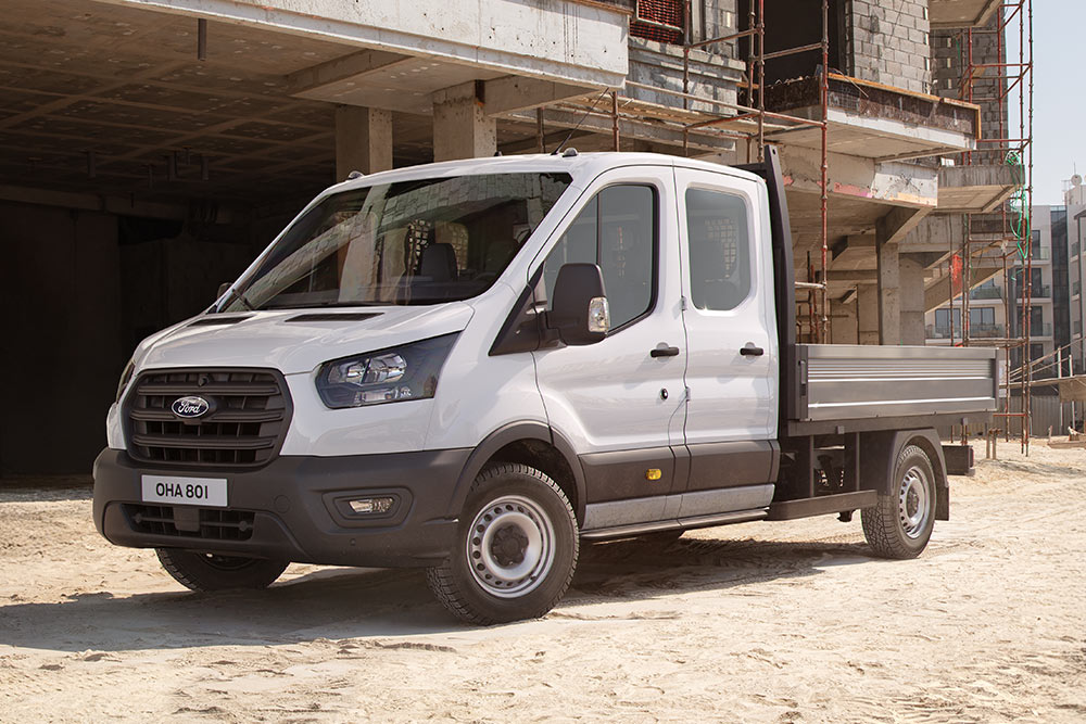  Fehér Ford Transit Custom alvázas fülke platóval parkol egy építkezésen.