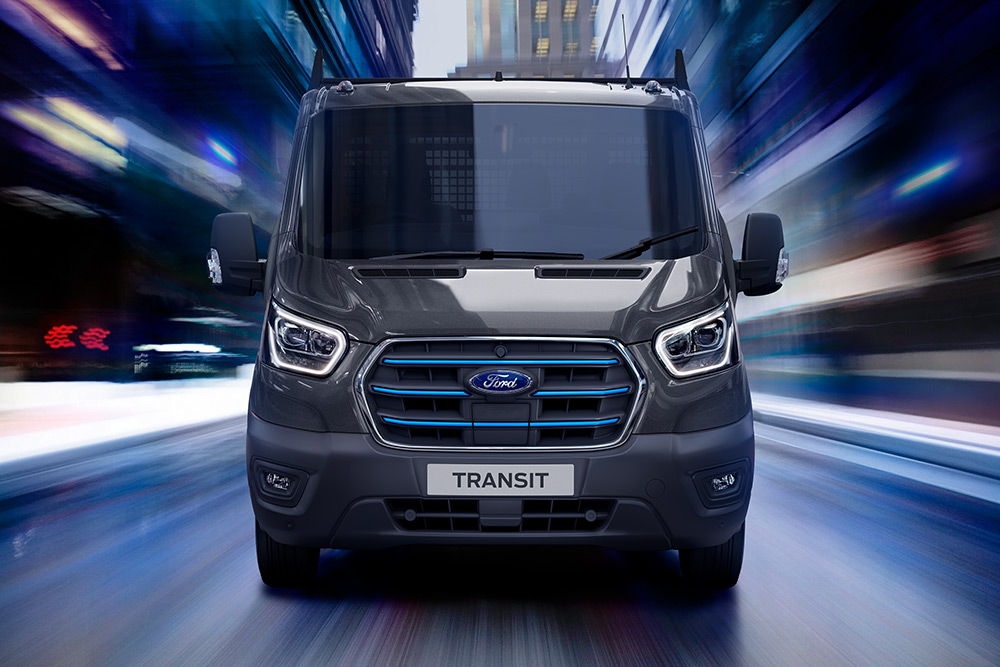   Egy sötétszürke Ford Transit furgon elölnézete mozgásban, elmosódott háttérrel.