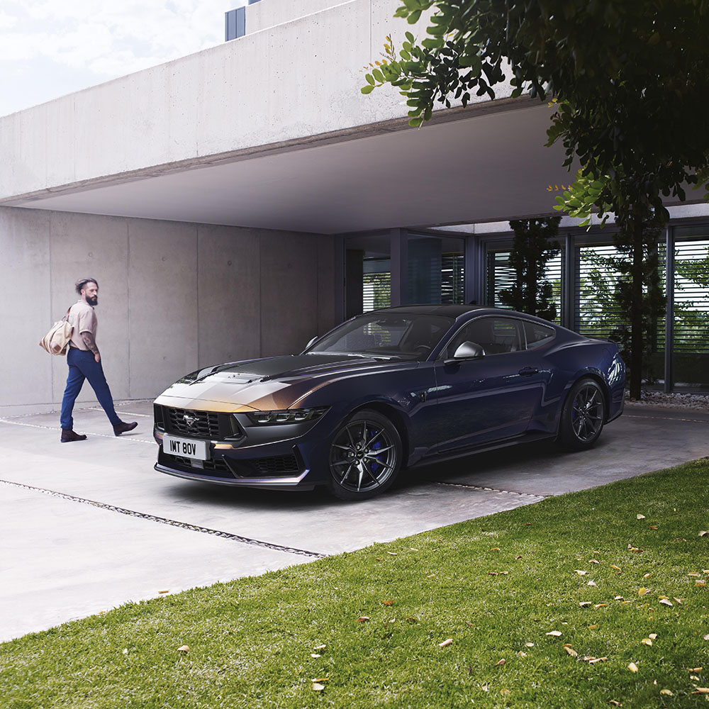 Kék Ford Mustang parkol egy felhajtón, mellette egy ember sétál el.